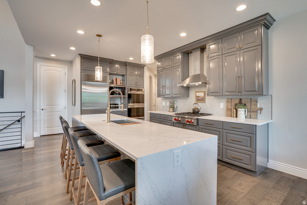Gourmet kitchen featuring an oversized island with countertop seating, light-toned countertops, gray cabinetry with crown molding, stainless steel appliances, and wood-finish flooring