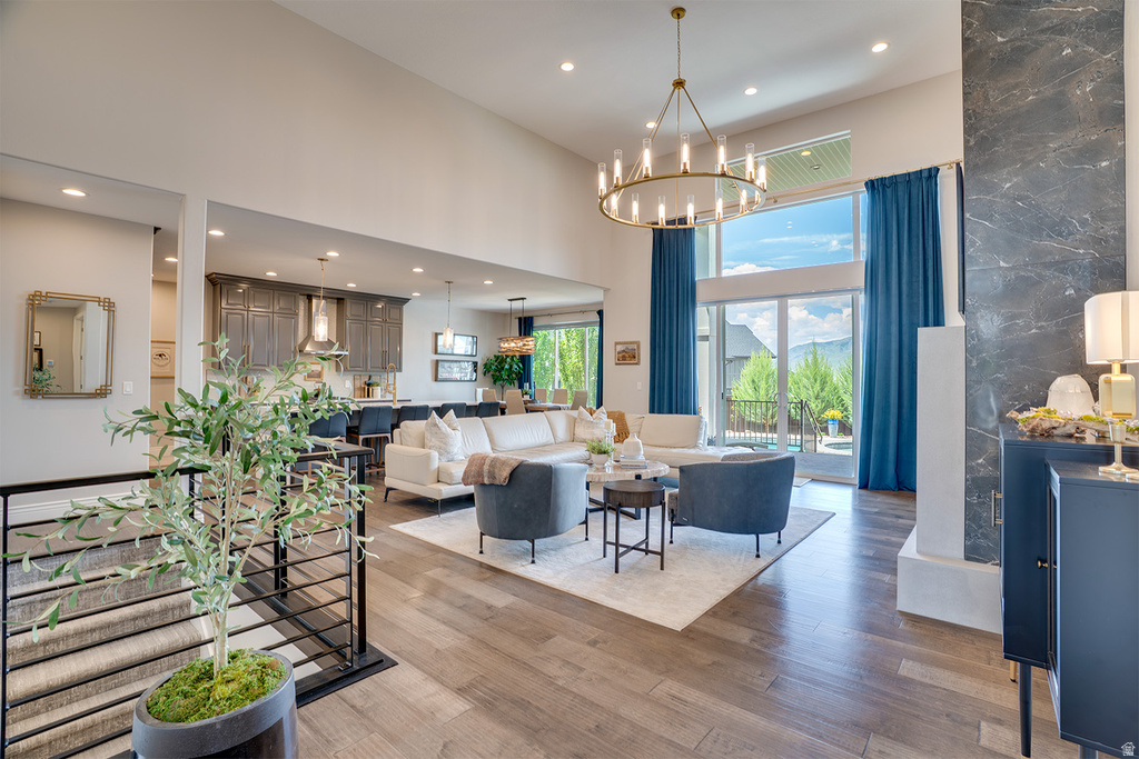 Open-concept living space featuring high ceilings, wood-finish flooring, a contemporary chandelier, and a floor-to-ceiling glass door