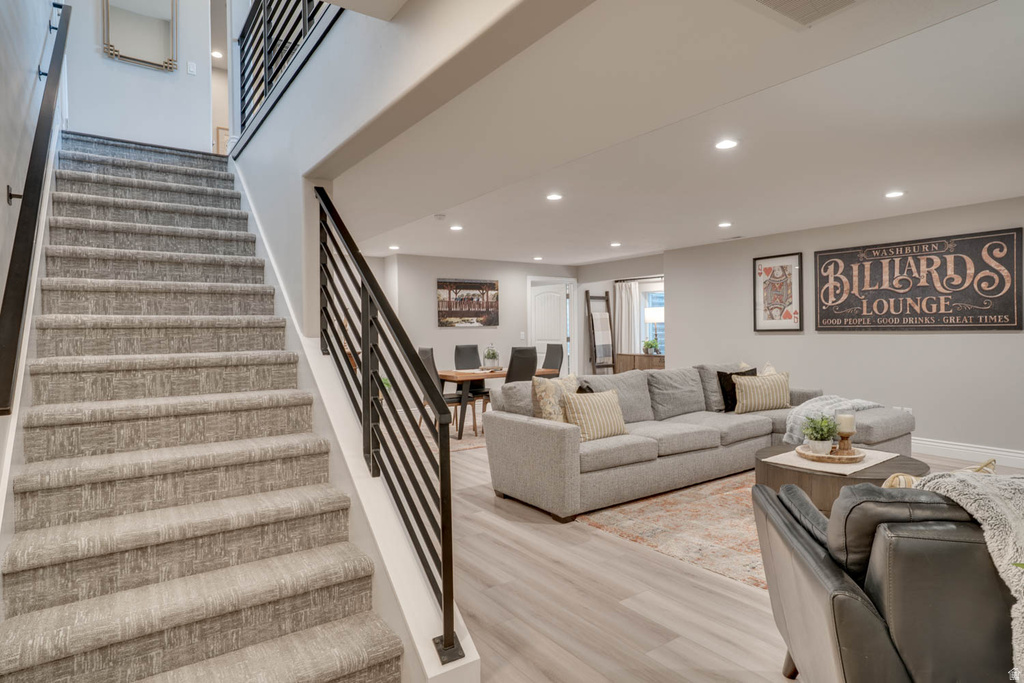 Carpeted staircase with black metal railings, recessed lighting, wood-finish flooring, and a dining area