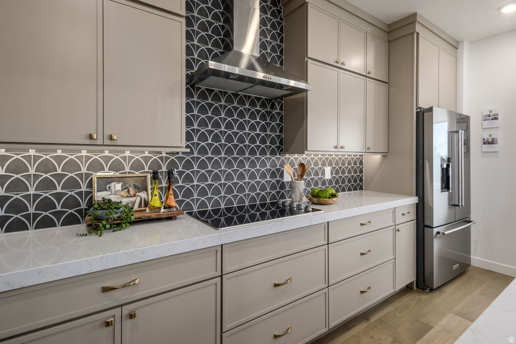 Kitchen featuring a distinctive scallop pattern tile backsplash, light-toned cabinetry with gold-toned hardware, stainless steel appliances, a built-in cooktop, and wood-finish flooring