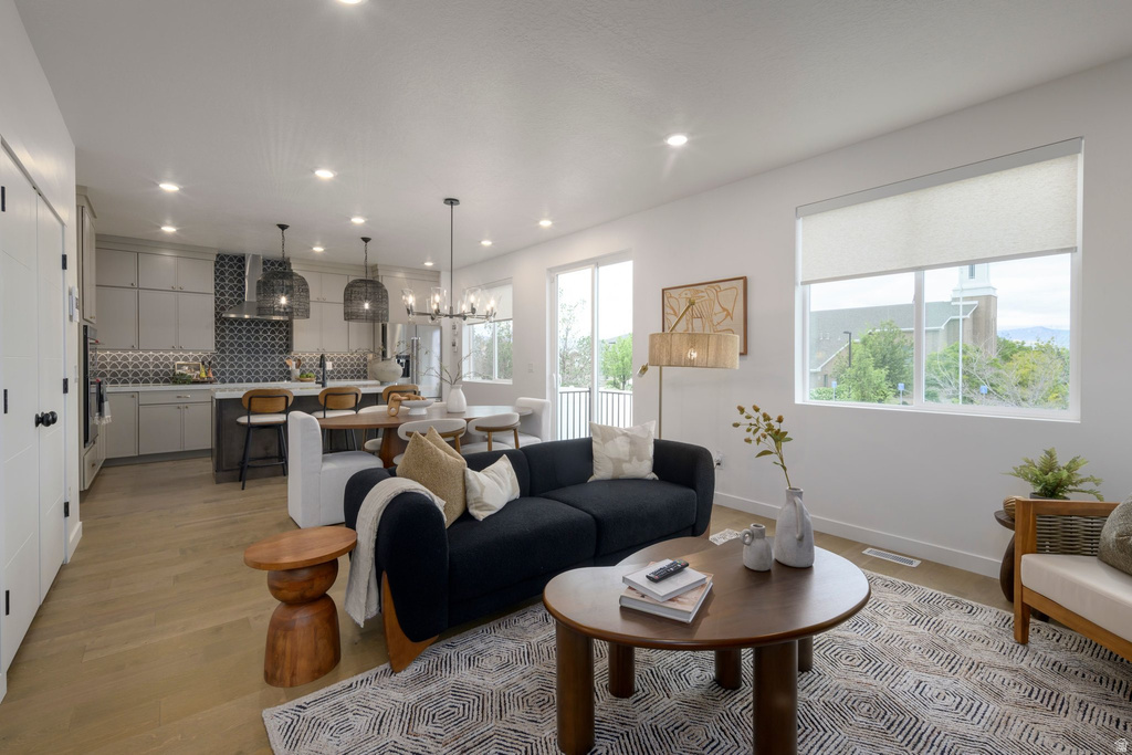 Open-concept living space featuring wood-finish flooring, recessed lighting, and a kitchen with light-toned cabinetry and a patterned tile backsplash