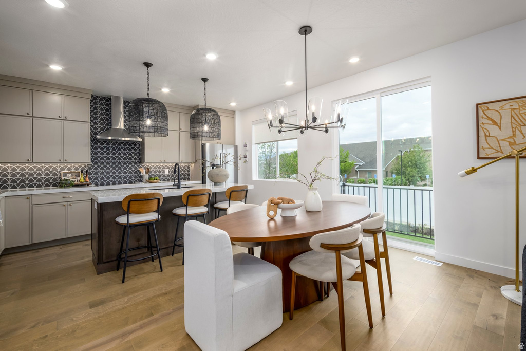 Open-concept living space featuring wood-finish flooring, a contemporary dining area with a modern chandelier, and a kitchen with light-toned cabinetry and a decorative tile backsplash