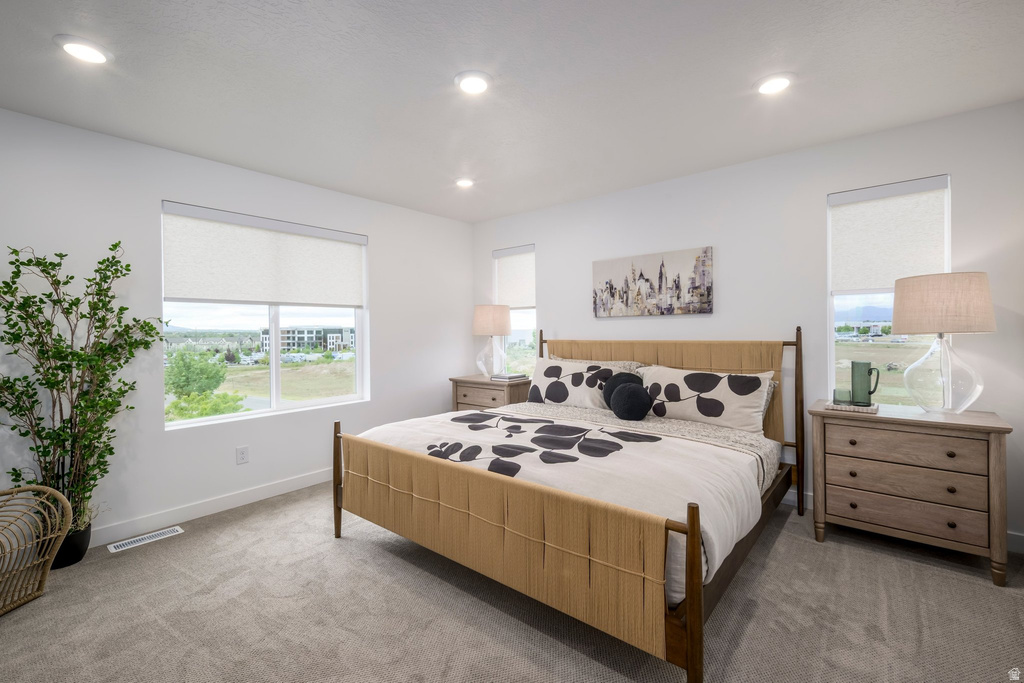 Bright bedroom featuring two large windows with roller shades, recessed lighting, and soft gray carpet flooring
