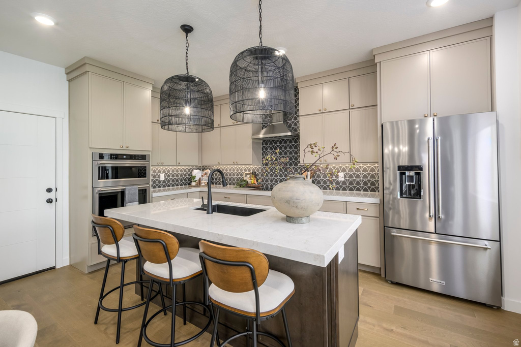 Kitchen featuring a central island with a light-toned countertop, stainless steel appliances, built-in double ovens, light-toned cabinetry, and a patterned backsplash