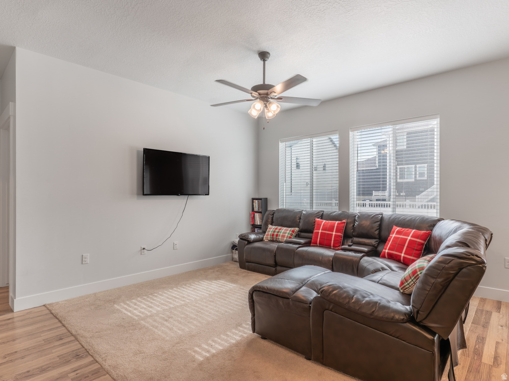 Living area featuring multiple windows with blinds, wood-finish flooring, and a ceiling fan with integrated lighting
