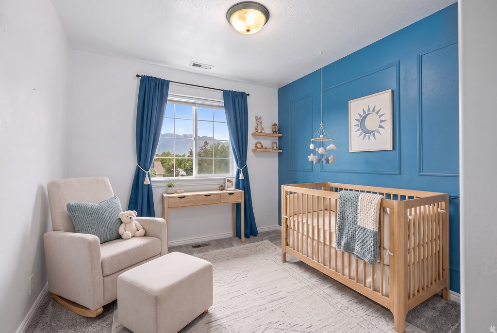 Bedroom featuring a decorative accent wall, a large window with white trim, and light wood-finish flooring