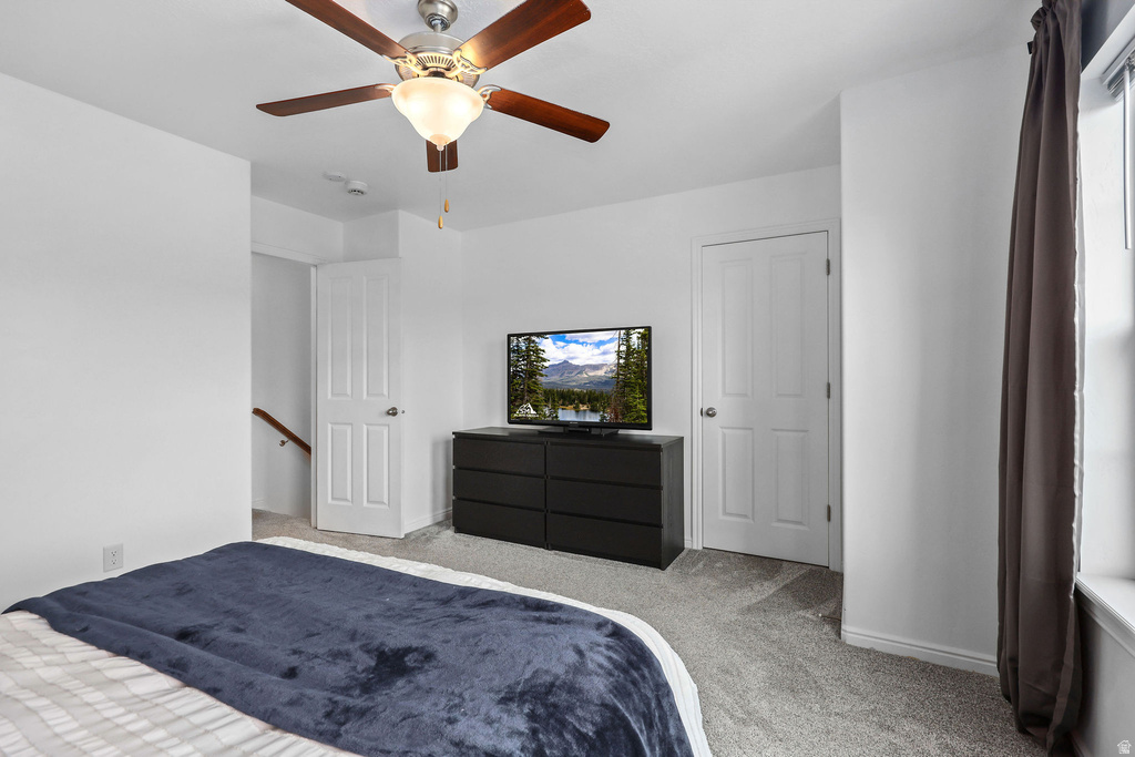 Carpeted interior with a ceiling fan, white walls, and a window
