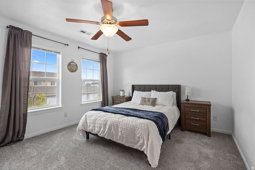Bedroom featuring neutral carpeting, a ceiling fan with light fixture, and two window openings