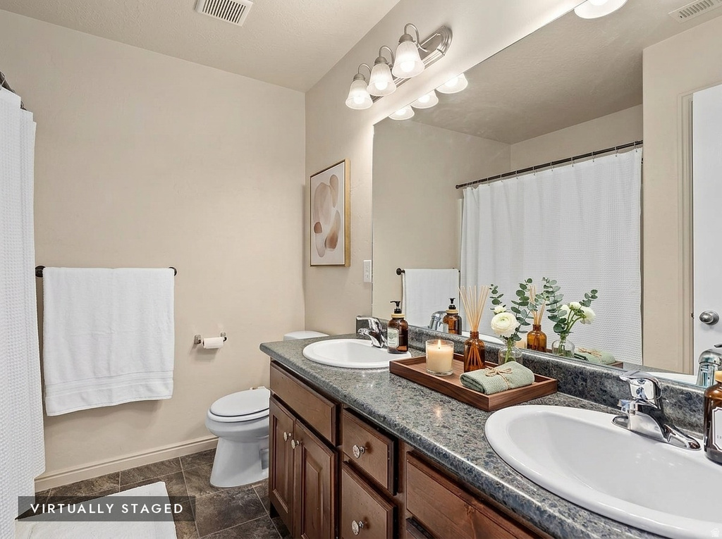 Dual vanity with integrated sinks, a wide mirror, sconce lighting, and wood-finish cabinetry
