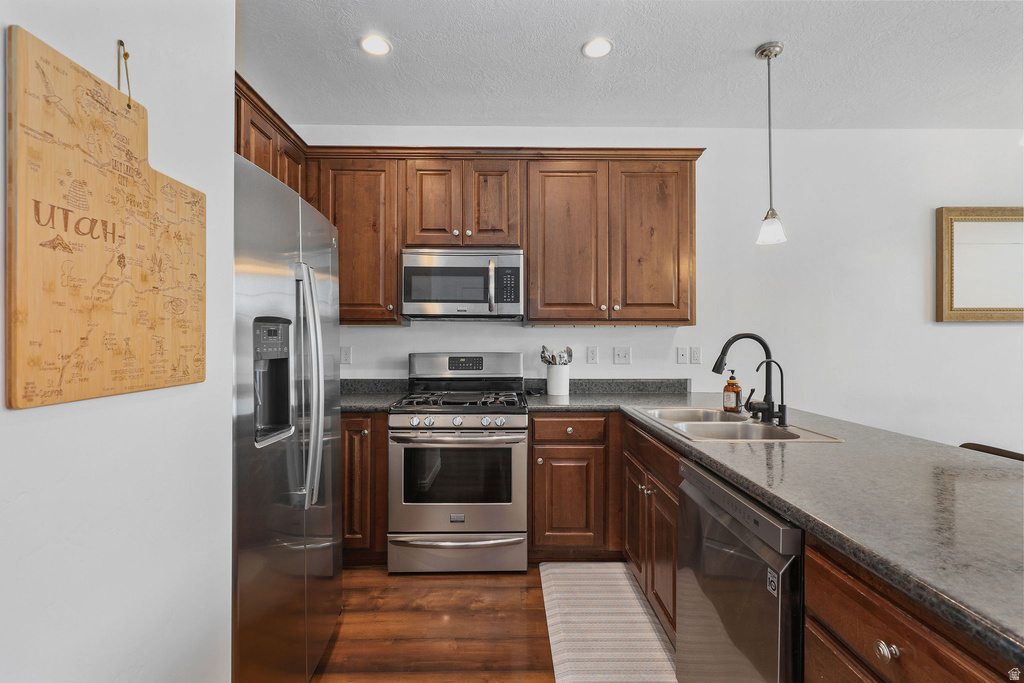 Modern kitchen featuring stainless steel appliances, dark wood cabinetry, a double basin sink with a black gooseneck faucet, gray countertops, and wood-finish flooring