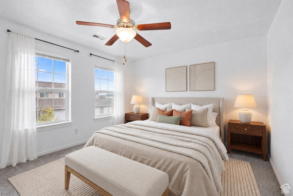 Bedroom featuring two large windows, a ceiling fan with light fixture, light gray carpeting, and white walls