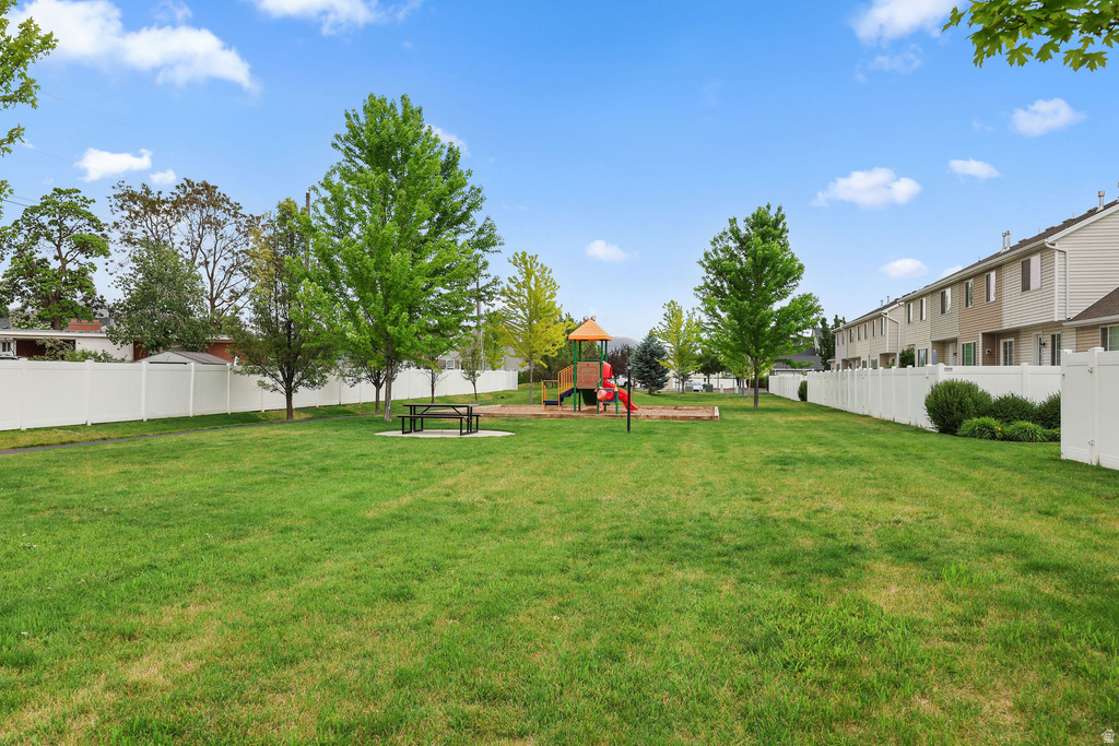 Expansive green lawn area featuring a dedicated playground structure, a picnic table on a concrete pad, and mature trees providing natural shading