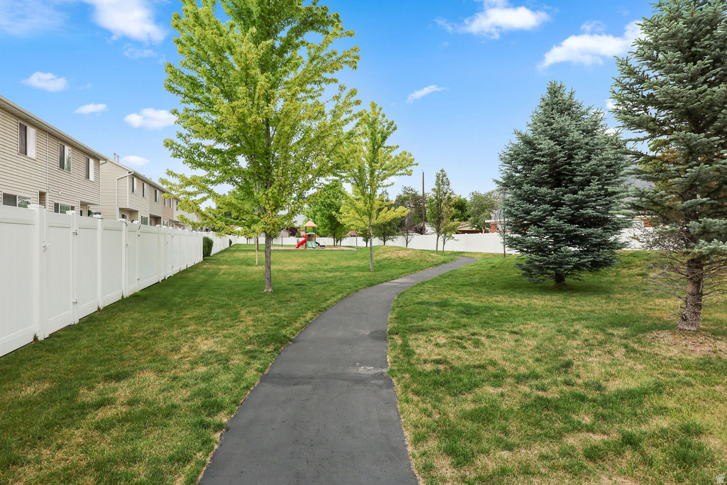 Expansive green space featuring a paved walking path, mature evergreen trees, and vibrant deciduous trees, bordered by a white privacy fence