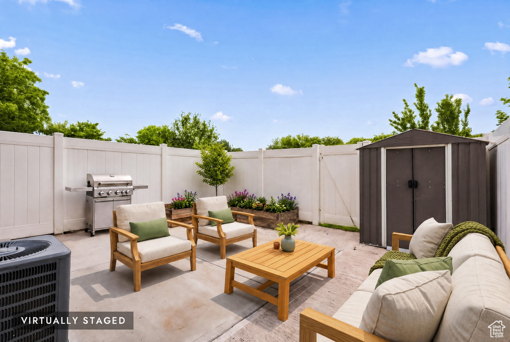 Outdoor patio space featuring concrete surfacing, a white privacy fence, a storage shed, and planter boxes with greenery