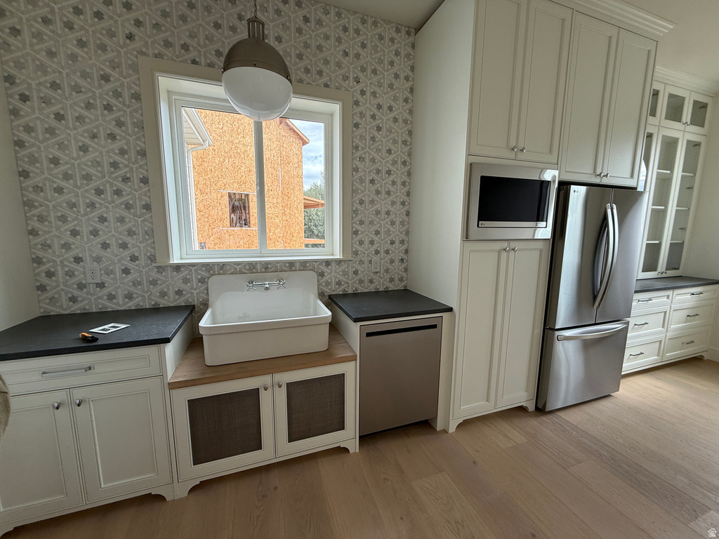 White shaker cabinetry, stainless steel appliances, dark countertops, patterned wall tile, and light wood-finish flooring