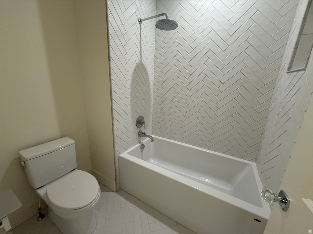 White subway tile in a herringbone pattern, rainfall shower head, chrome shower and tub fixtures, white soaking tub, and white toilet