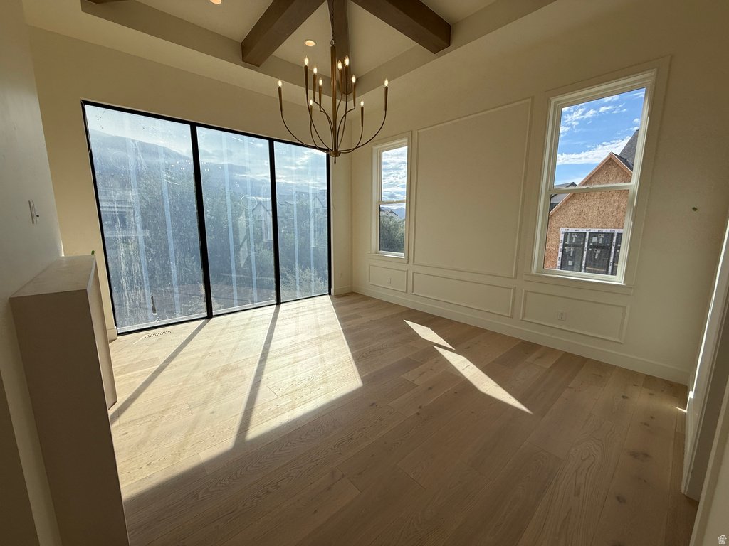 Vaulted ceiling with exposed wood beams, wood-finish flooring, large multi-pane windows, decorative wall molding, and a chandelier with candelabra bulbs
