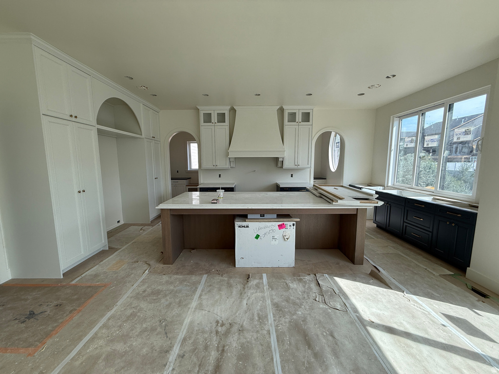 Central kitchen island with a light-toned countertop, white upper cabinetry, built-in range hood, dark lower cabinetry, and recessed lighting
