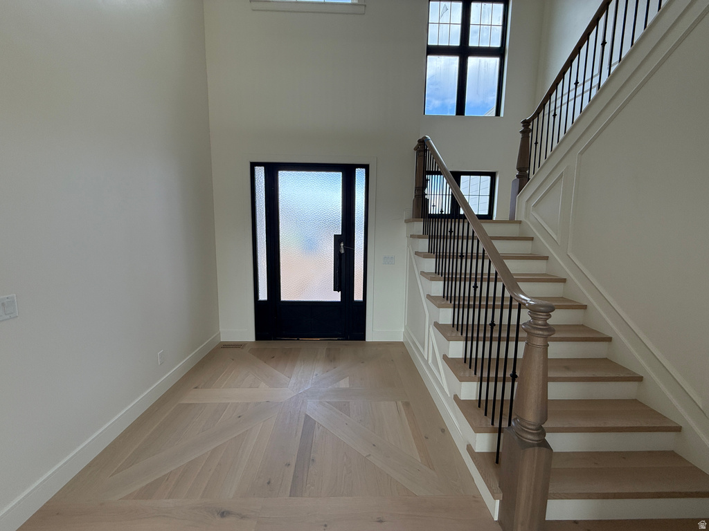 Two-story foyer featuring patterned wood-finish flooring, a grand staircase with wrought iron balusters, a dark-frame entry door with frosted glass, and transom windows