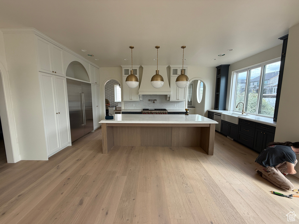 Gourmet kitchen featuring a large central island with white countertop, integrated stainless steel appliances, light wood-finish flooring, and white and dark cabinetry