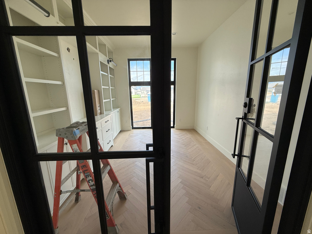Herringbone pattern wood-finish flooring, built-in cabinetry with shelving, black-framed glass doors, and black-framed windows