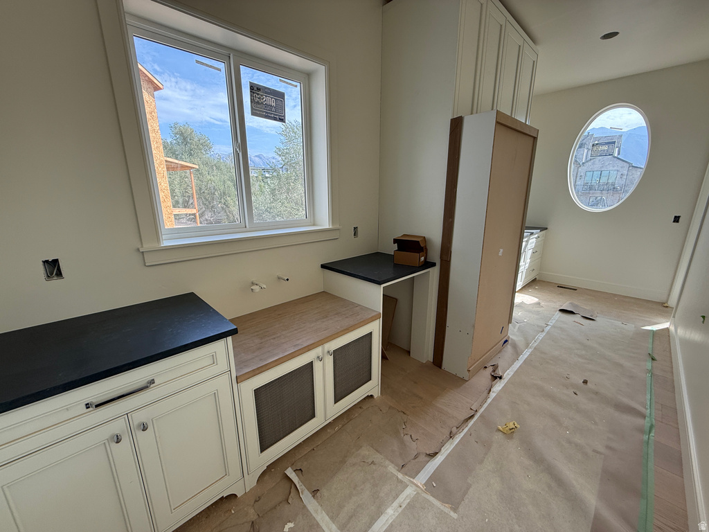White shaker-style cabinetry with dark countertops, built-in storage bench with wood-finish top, large rectangular window, and oval window