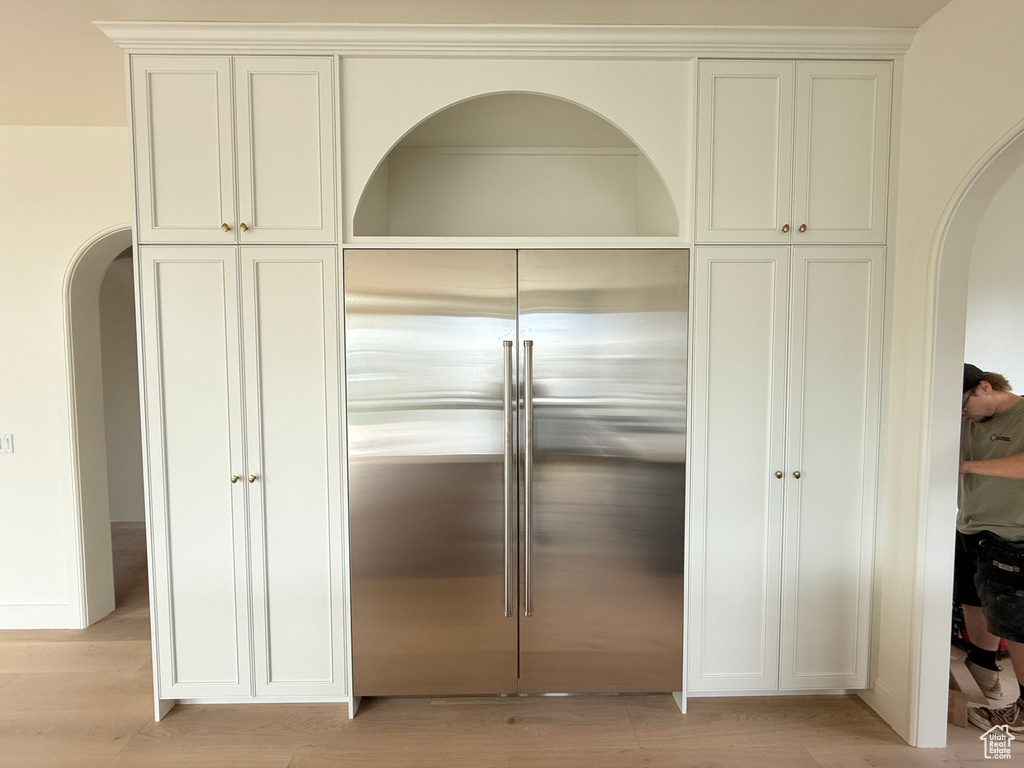 Built-in paneled cabinetry with gold-tone hardware, integrated stainless steel refrigerator, arched alcove, and crown molding