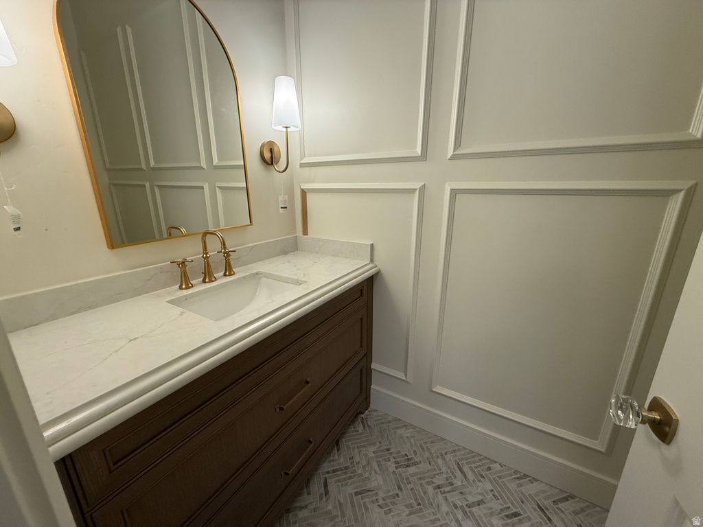 Wood vanity with a white countertop and integrated sink, gold-tone faucet, arched mirror, and wall sconces