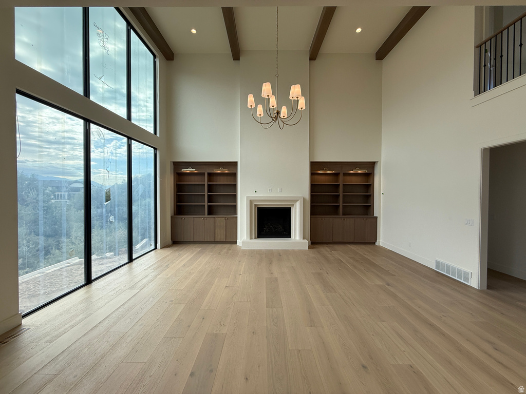 Double-height ceilings with exposed wood beams, extensive floor-to-ceiling windows, wood-finish flooring, a built-in fireplace with a mantel, and integrated shelving units with cabinet storage