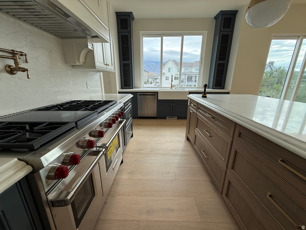 Kitchen featuring light wood-finish flooring, a large central island with a light-toned countertop, and dark-toned cabinetry with light hardware