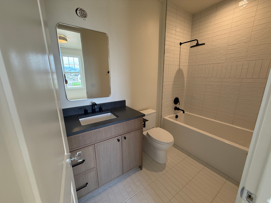 Modern bathroom featuring a wood-finish vanity with an integrated sink and dark countertop, a rectangular mirror, a toilet, a bathtub with a matte black shower fixture, and tiled flooring