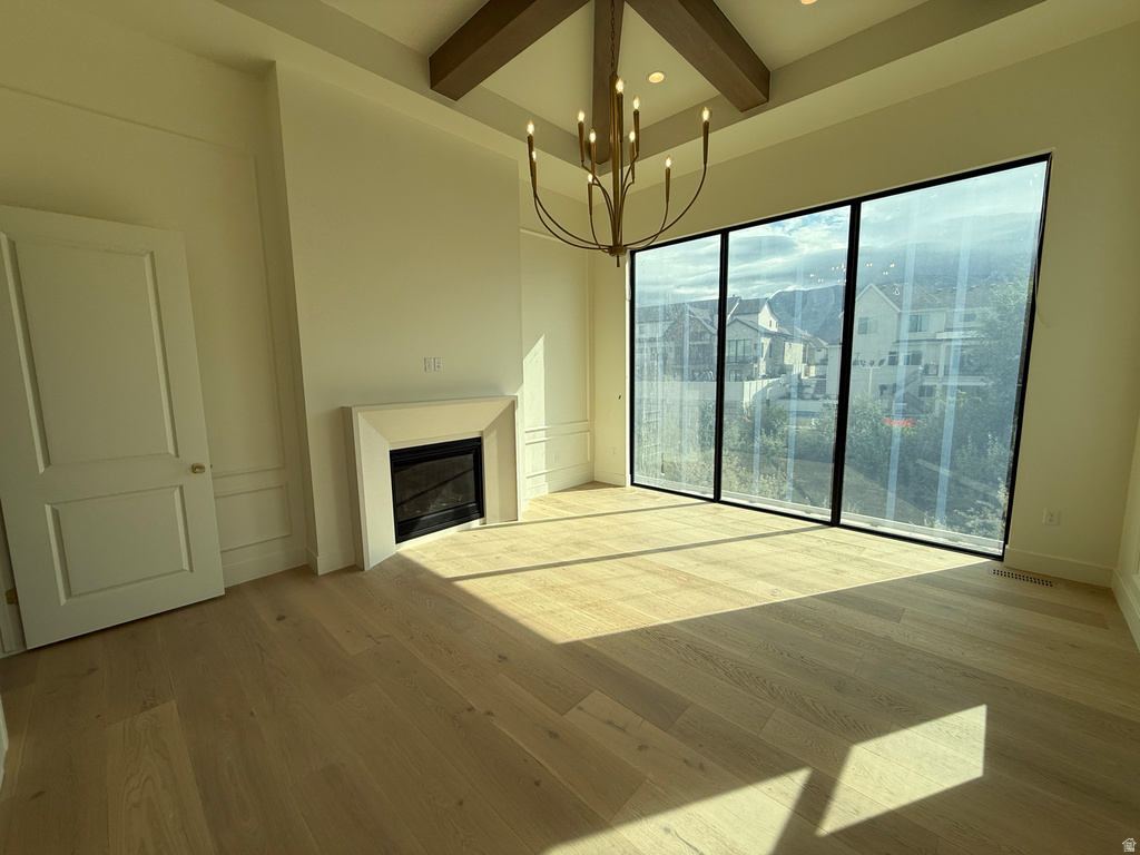 Spacious room featuring wood-finish flooring, a contemporary chandelier, a built-in fireplace with a mantel, and panel wall detailing