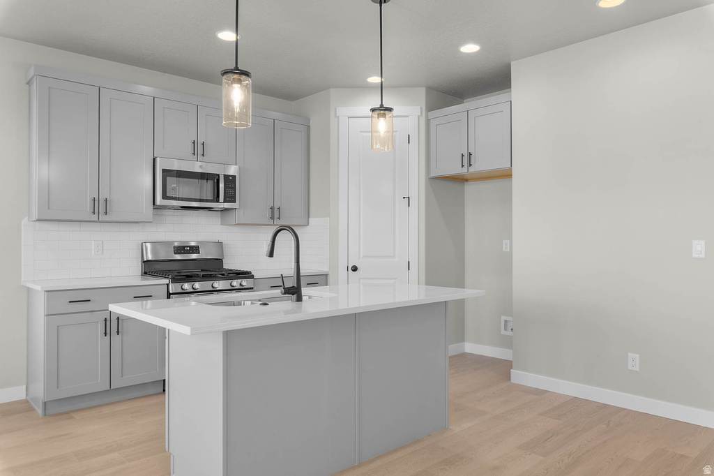 Modern kitchen featuring grey shaker-style cabinetry, a white subway tile backsplash, and stainless steel appliances