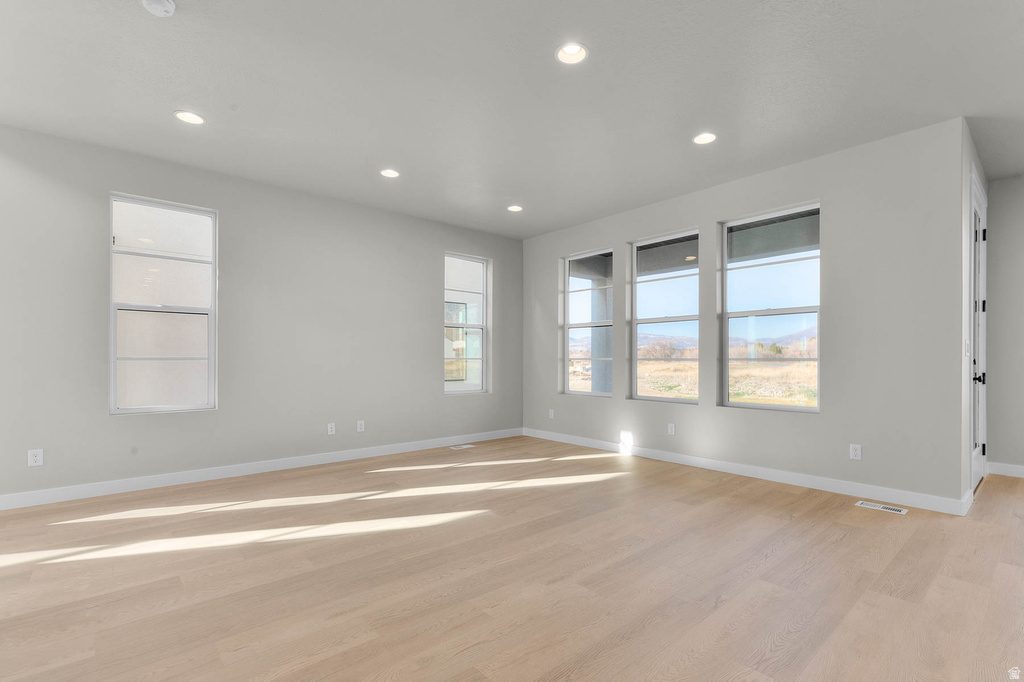 Spacious room featuring light-toned wood-finish flooring and recessed lighting