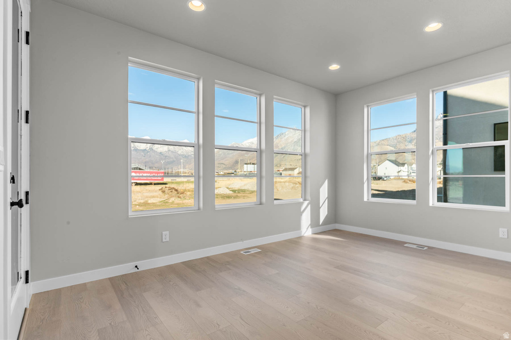 Expansive room with five large windows, light wood-finish flooring, recessed lighting, white baseboards, and a white interior door with black hardware