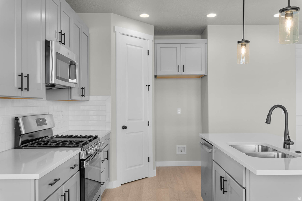 Modern kitchen featuring light gray cabinetry with black hardware, white countertops, stainless steel appliances, a subway tile backsplash, and light wood-finish flooring