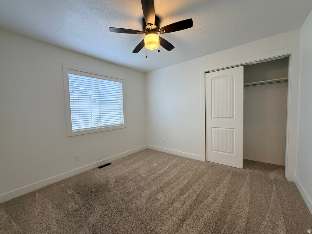 Bedroom featuring neutral tone carpeting, a window with horizontal blinds, a ceiling fan with light fixture, and a closet with a bi-fold paneled door