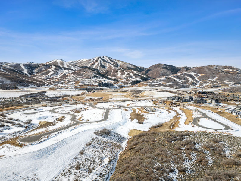 Expansive snow-covered landscape featuring a mountain range backdrop, winding roads, and distant residential structures