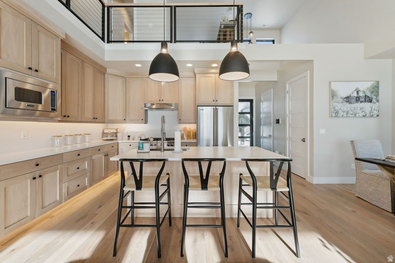 Modern kitchen featuring light wood-finish cabinetry, stainless steel appliances, and a central island with countertop seating