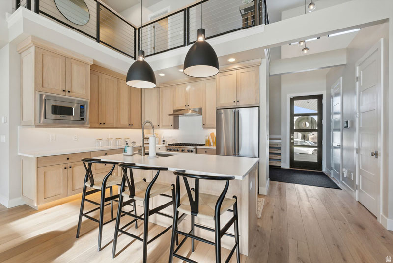 Modern kitchen featuring light wood cabinetry, stainless steel appliances, and a central island with a light-toned countertop