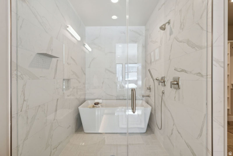 Glass-enclosed wet room featuring a freestanding soaking tub and two distinct shower systems