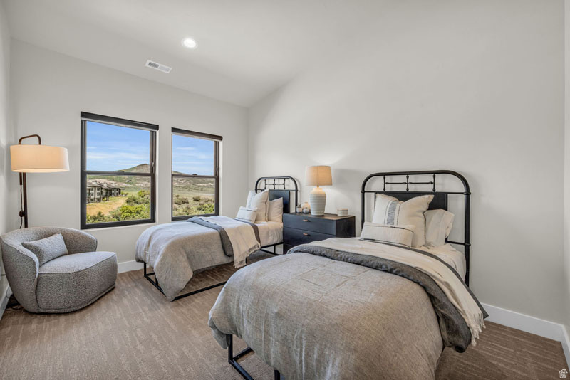 Bedroom featuring two windows showcasing mountain scenery, light-toned carpeting, white walls, recessed lighting, and white baseboards