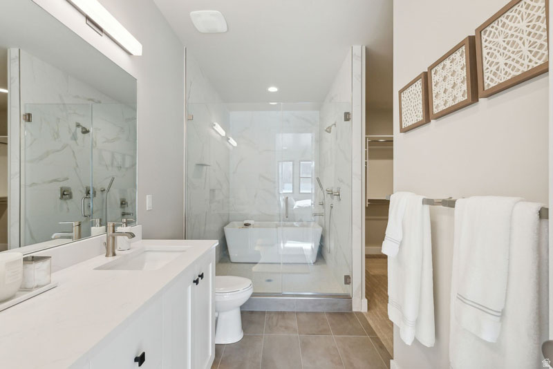 Bathroom featuring a freestanding soaking tub, enclosed glass shower with marble-look tile, single vanity with light-colored countertop, and a brushed nickel faucet