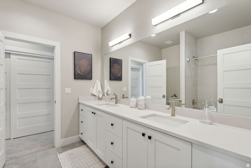 Spacious bathroom featuring a dual vanity with white cabinetry, integrated sinks, and brushed nickel faucets