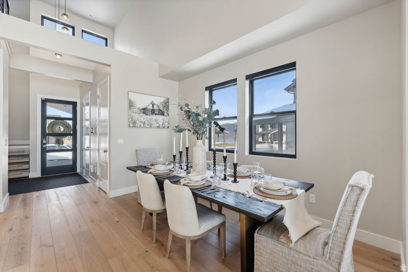 Open-concept dining area featuring light wood-finish flooring, a vaulted ceiling, and multiple windows with black trim