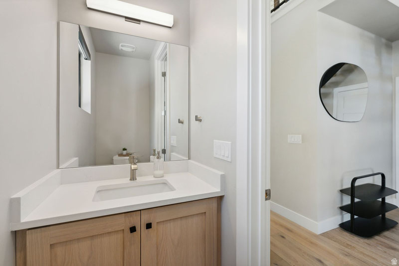 Modern bathroom vanity featuring light wood cabinetry with black hardware, a white countertop, and an undermount sink