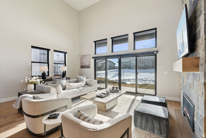 Spacious living area featuring a stacked stone fireplace with a wood mantel, high ceilings, wood-finish flooring, and expansive sliding glass doors