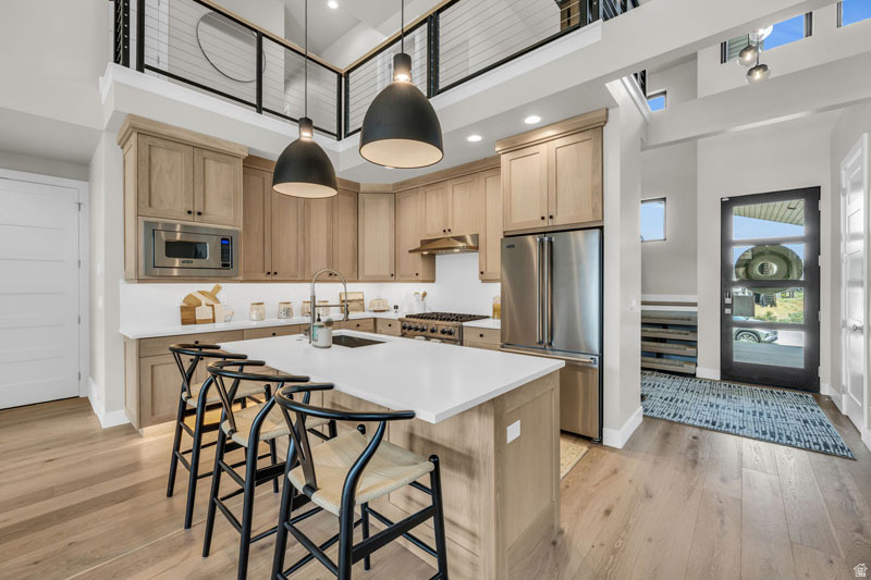Contemporary kitchen featuring light wood-finish cabinetry, stainless steel appliances, a center island with seating, and wood-finish flooring