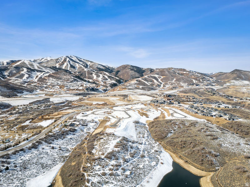 Expansive mountain landscape featuring snow-covered peaks, a residential development, and a body of water