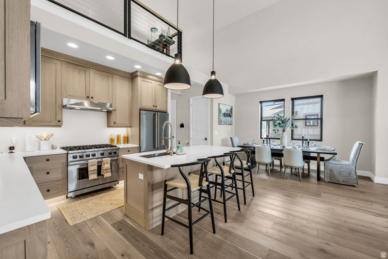 Open-concept kitchen and dining area featuring light wood-finish cabinetry, stainless steel appliances, and wood-finish flooring
